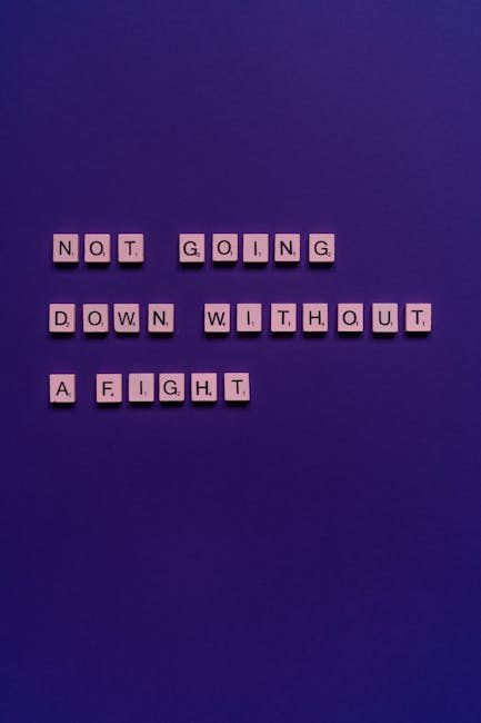 A photograph showing letter tiles arranged on a solid purple background displaying the phrase 'NOT GOING DOWN WITHOUT A FIGHT'. The tiles are evenly spaced in a grid-like pattern, with each letter on a small square tile. The image does not include any furniture, boxes, or moving equipment; it is centered solely on the message conveyed by the tiles, which may relate metaphorically to a home relocation or packing and moving themes relevant to [COMPANY_NAME], Man with Van Holloway, and its house removal services. The lighting is uniform, with no shadows or reflections, emphasizing clarity and the visual message of determination and resilience in the context of moving or removals.