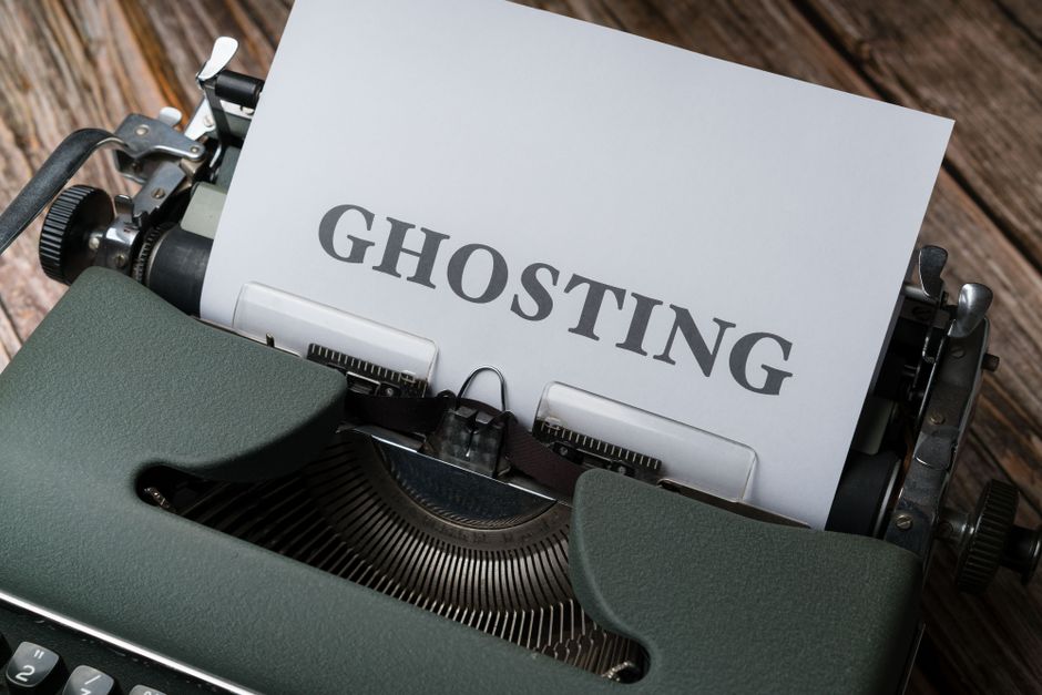 Close-up image of a dark wooden desk surface with scattered sheets of paper containing random print characters, a magnifying glass resting on top of the papers, and a few beige envelopes beneath. In the background, there is a black circular container holding several cigarettes and a small metallic object. The scene appears to be part of an indoor setting related to document handling or analysis, with natural ambient lighting. This setup may relate to packing or organizing items during a home relocation or moving process, as carried out by Man with Van Holloway, specializing in removals and furniture transport within the context of packing and moving services.